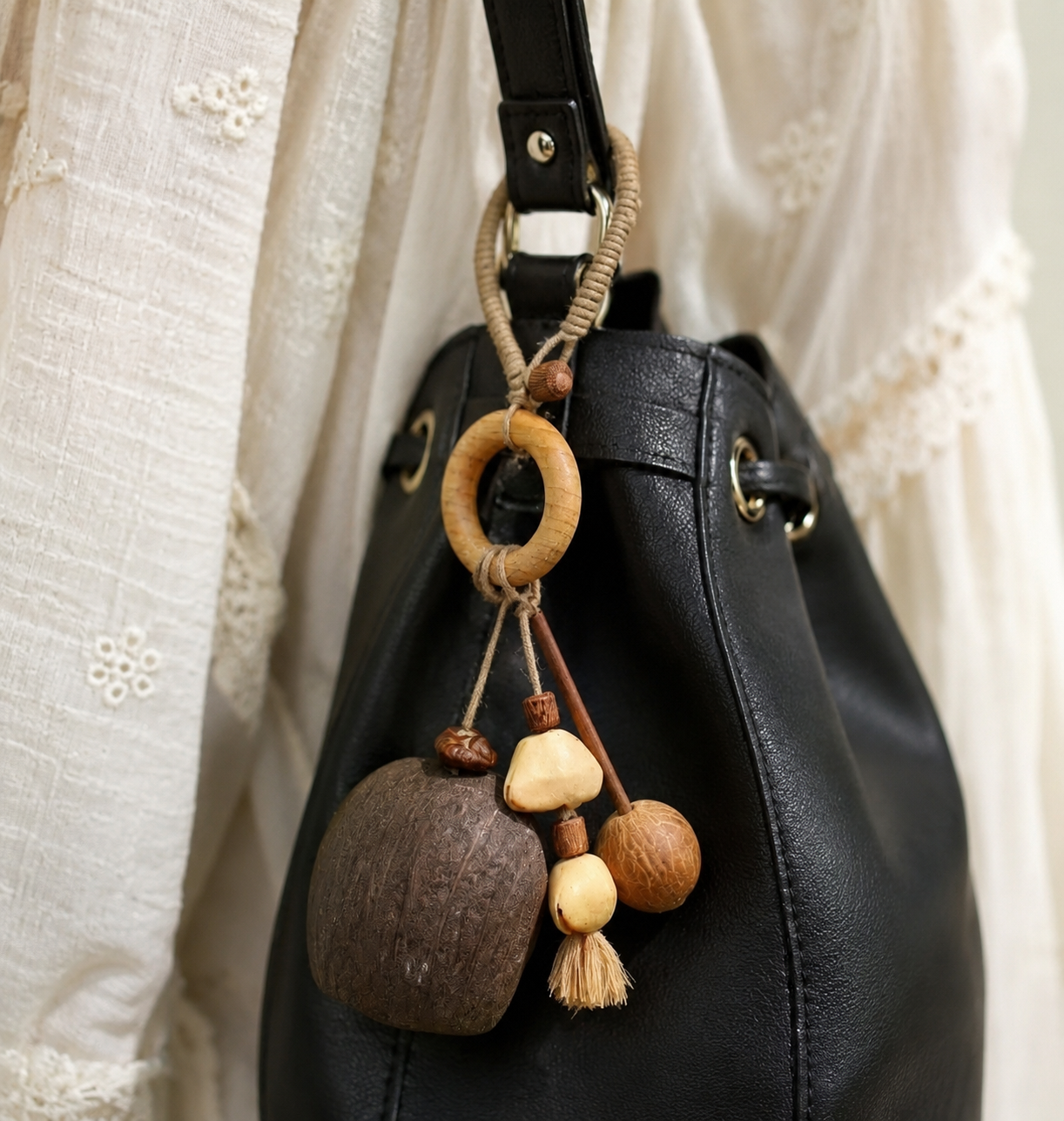 A portable nut shell wooden fish charm hanging on the side of a black leather bucket bag, showing its use as a stylish accessory