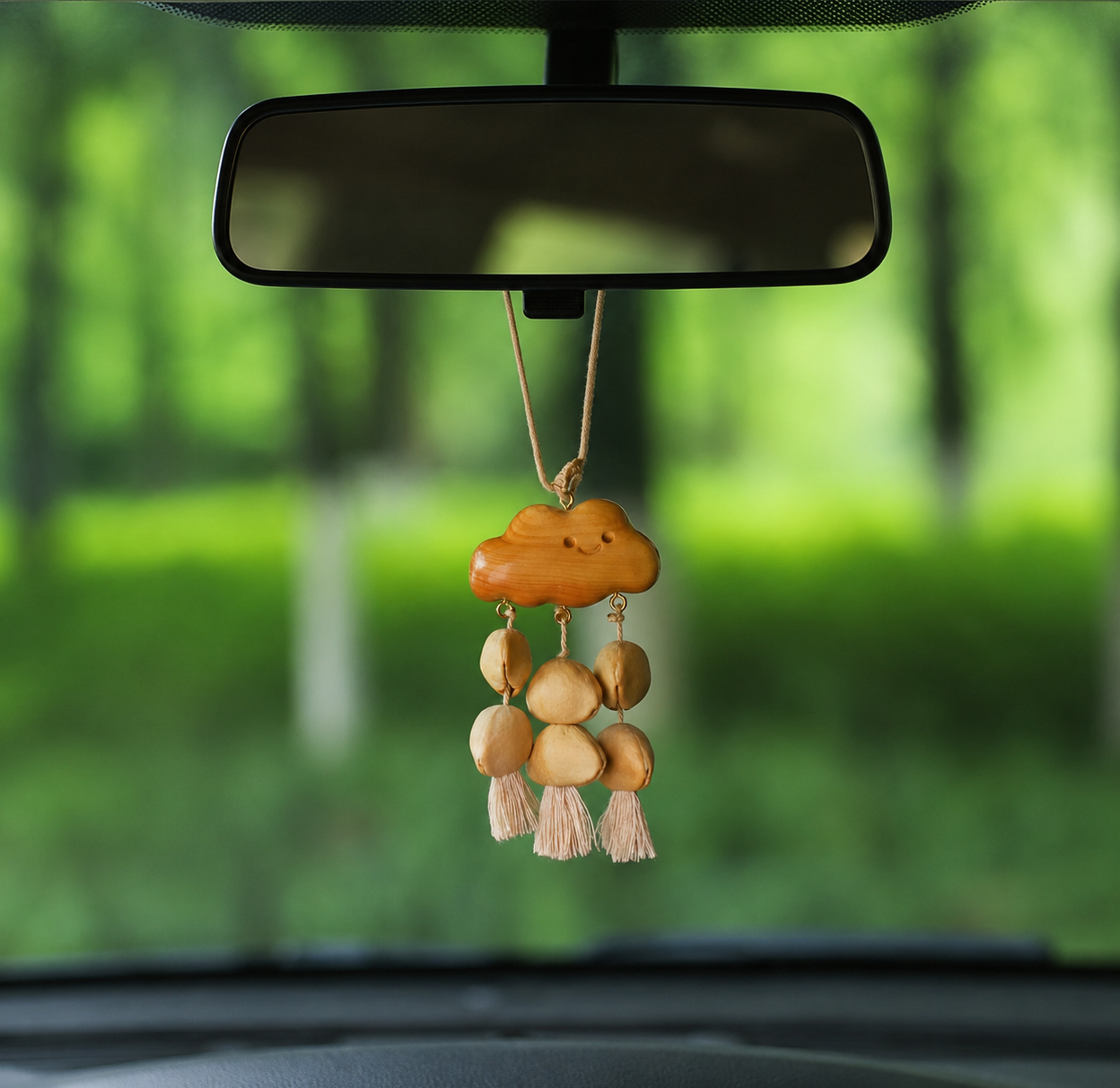 The "Rainy Cloud" natural shell and wood car charm hanging from a rearview mirror, showcasing its use as a healing and mindful car interior accessory