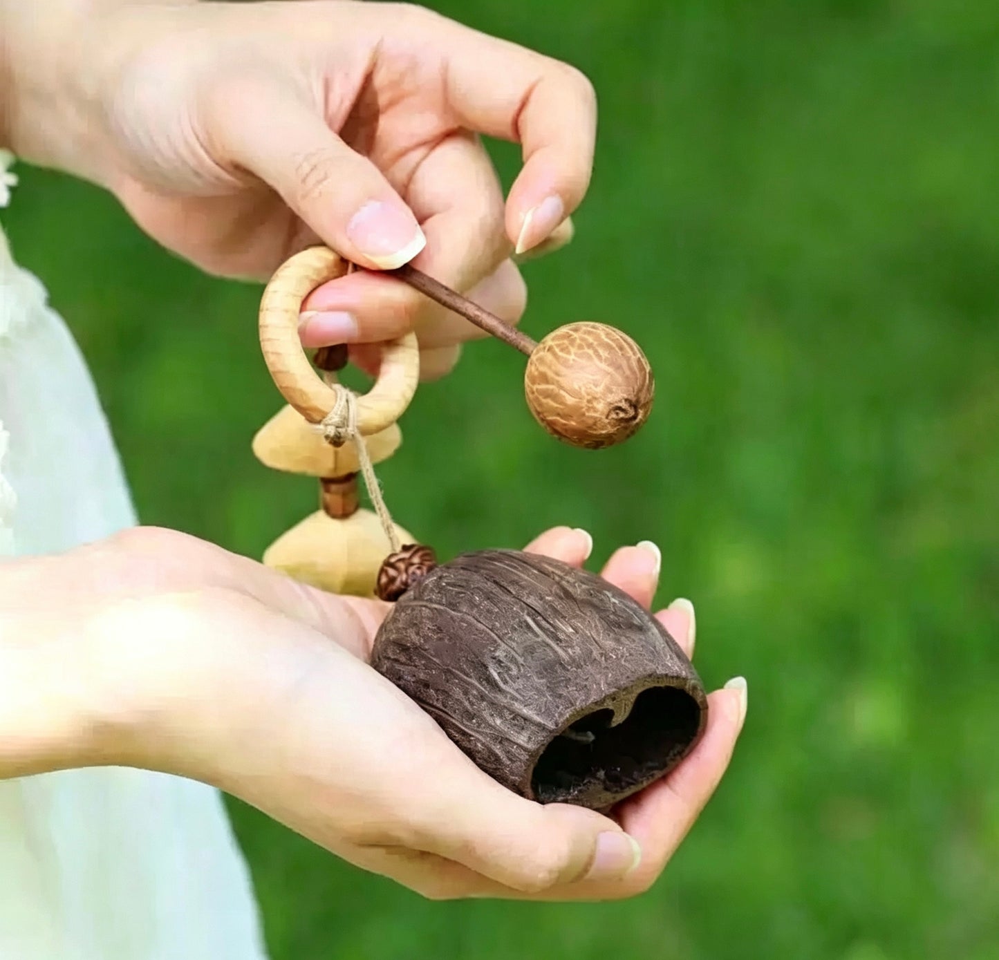 Close-up of hands holding a handmade natural nut shell wooden fish, showing the interaction between the striker and the shell base.