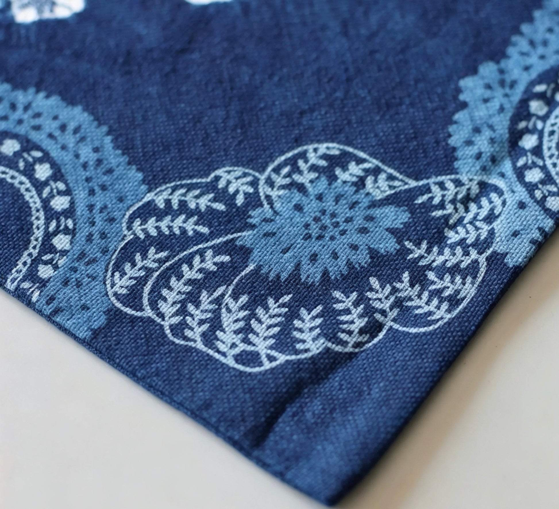 Close-up detail of the intricate blue floral and botanical tie-dye pattern on the corner of a handcrafted indigo cotton mat, showing fabric texture.