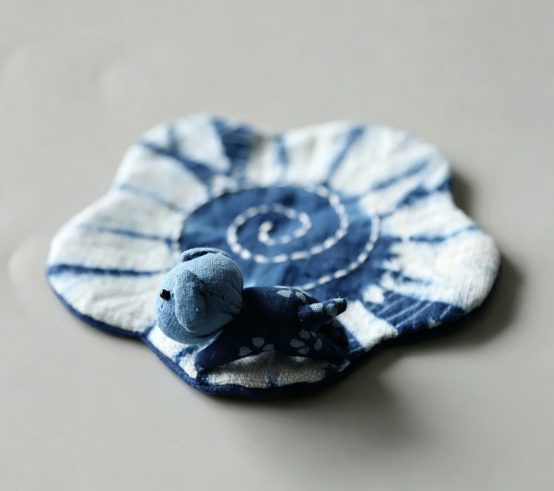 Close-up of a hand-sewn puppy indigo tie-dye desktop mat, handcrafted cotton fabric with blue and white ripple patterns, healing desk companion.