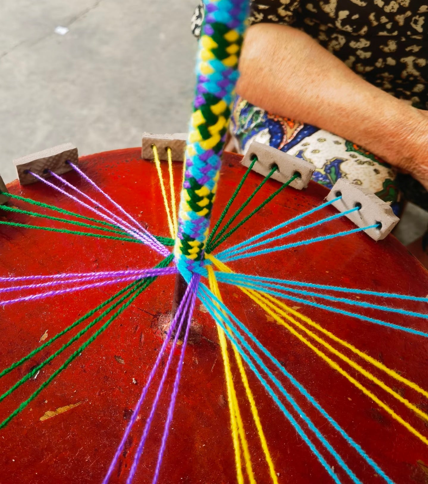 A traditional "Five-Color" weaving tool in use, surrounded by vibrant five-colored threads. This image captures the delicate process of integrating colorful cords with natural materials through heritage hand-weaving techniques.