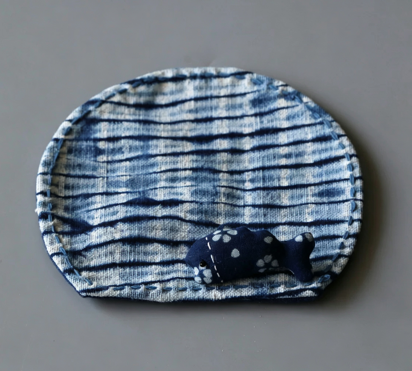 Hand-dyed fish-shaped indigo fabric mat with a small stuffed fish companion, traditional Yunnan tie-dye patterns in deep blue