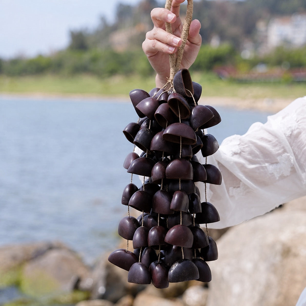 Handheld polished Juju shell wind chime with a serene lakeside backdrop, featuring smooth Juju shell for meditation and sound healing.