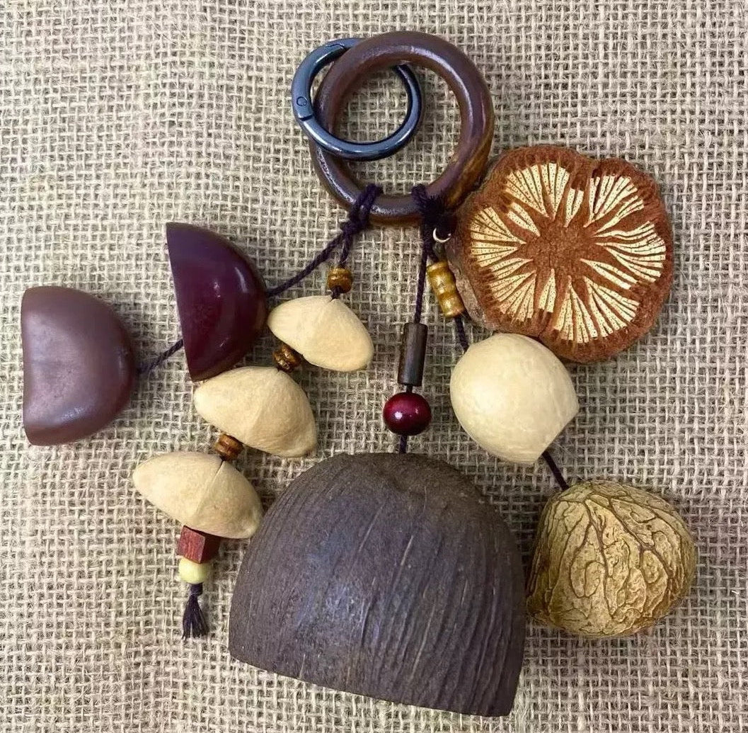 A flat-lay view of the hanging charm composed of natural nut shells, a wooden ring, and a floral disc on a rustic burlap textured background, showcasing its minimalist and organic artistic style.